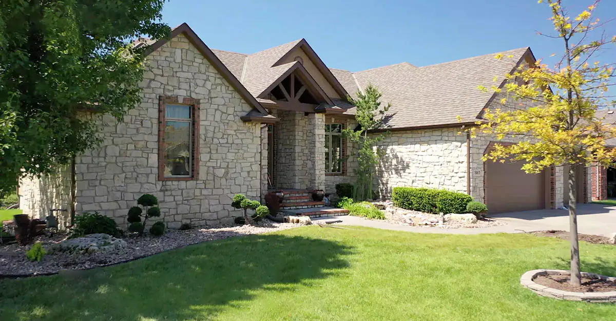 Green front lawn and trimmed shrubs at a stone home in Wichita maintained by Four Star Lawn Care